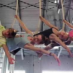 4 happy circus students on a triple trapeze